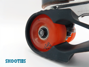 A black Skootie is looped over the inside back wheel of a black skate boot. The focus is on the back orange wheel, showing the way a Skootie loop cups the wheel.